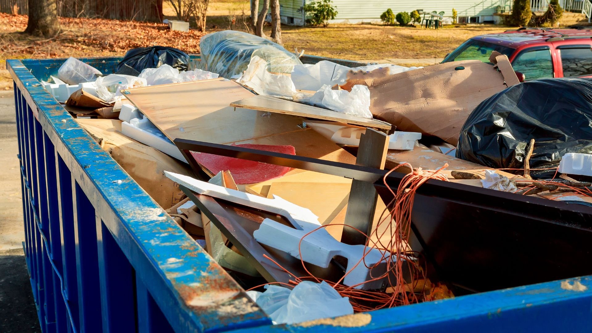Blue dumpster filled with construction debris, wood, and plastic bags