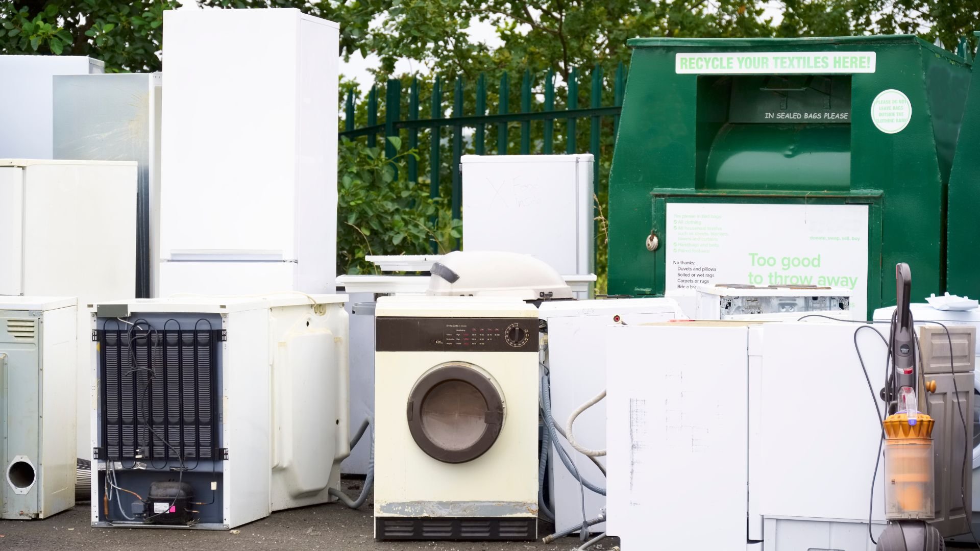 Discarded white appliances near textile recycling bin with green background