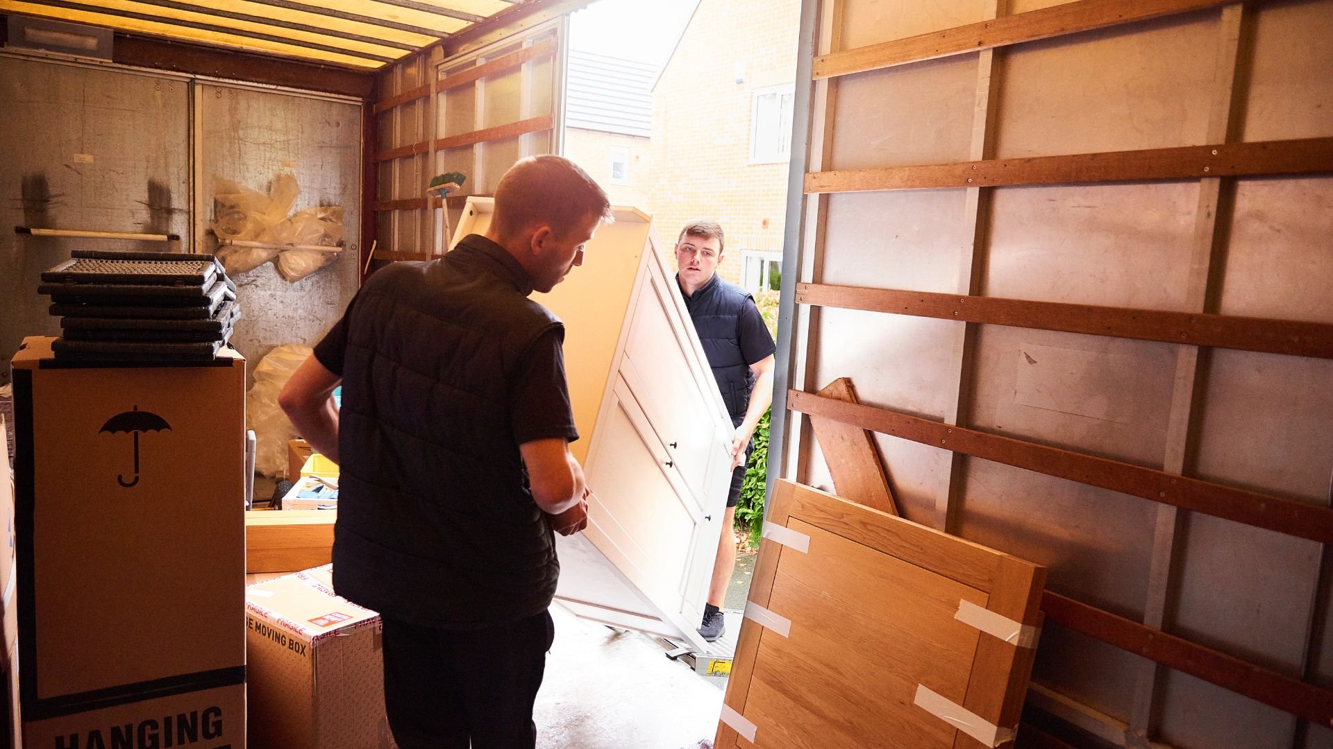 Two workers moving wooden boards inside a storage or moving truck