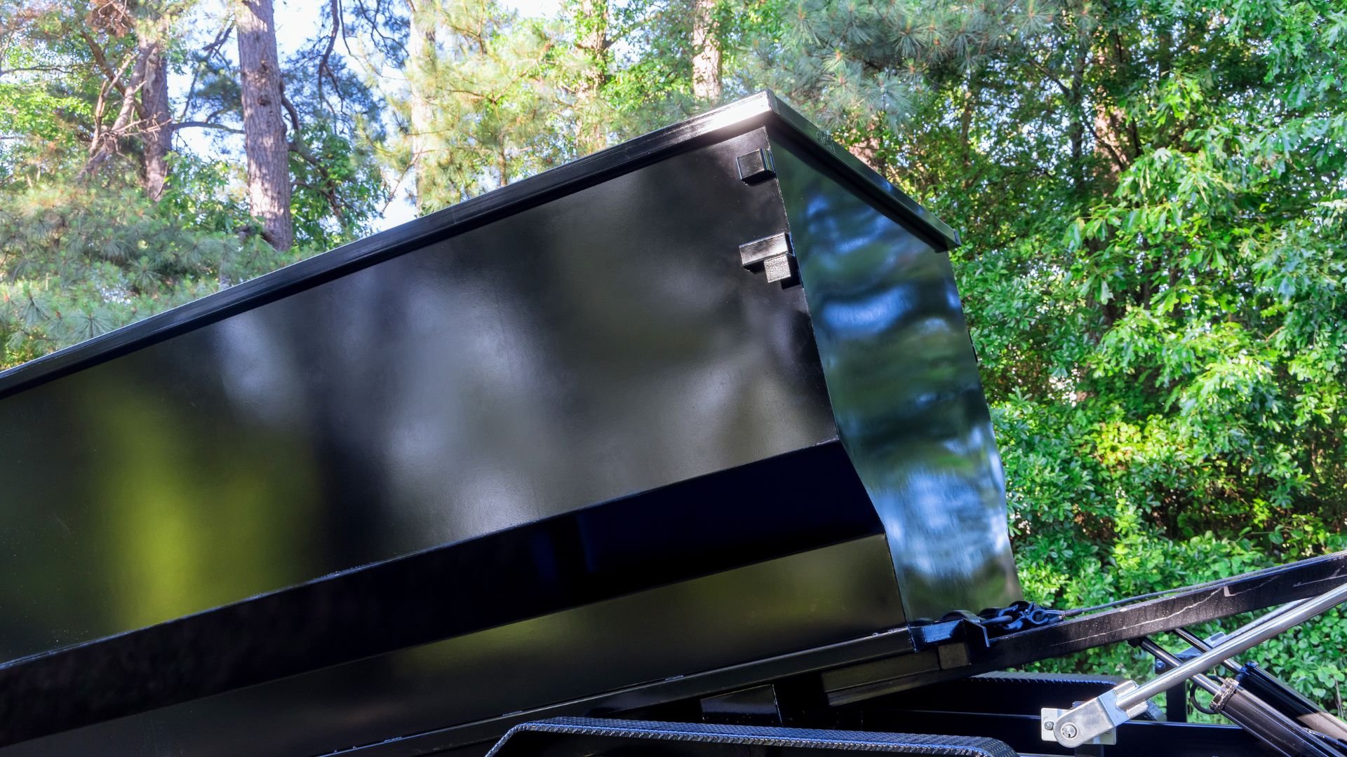 Black dumpster with open lid parked in wooded forest area