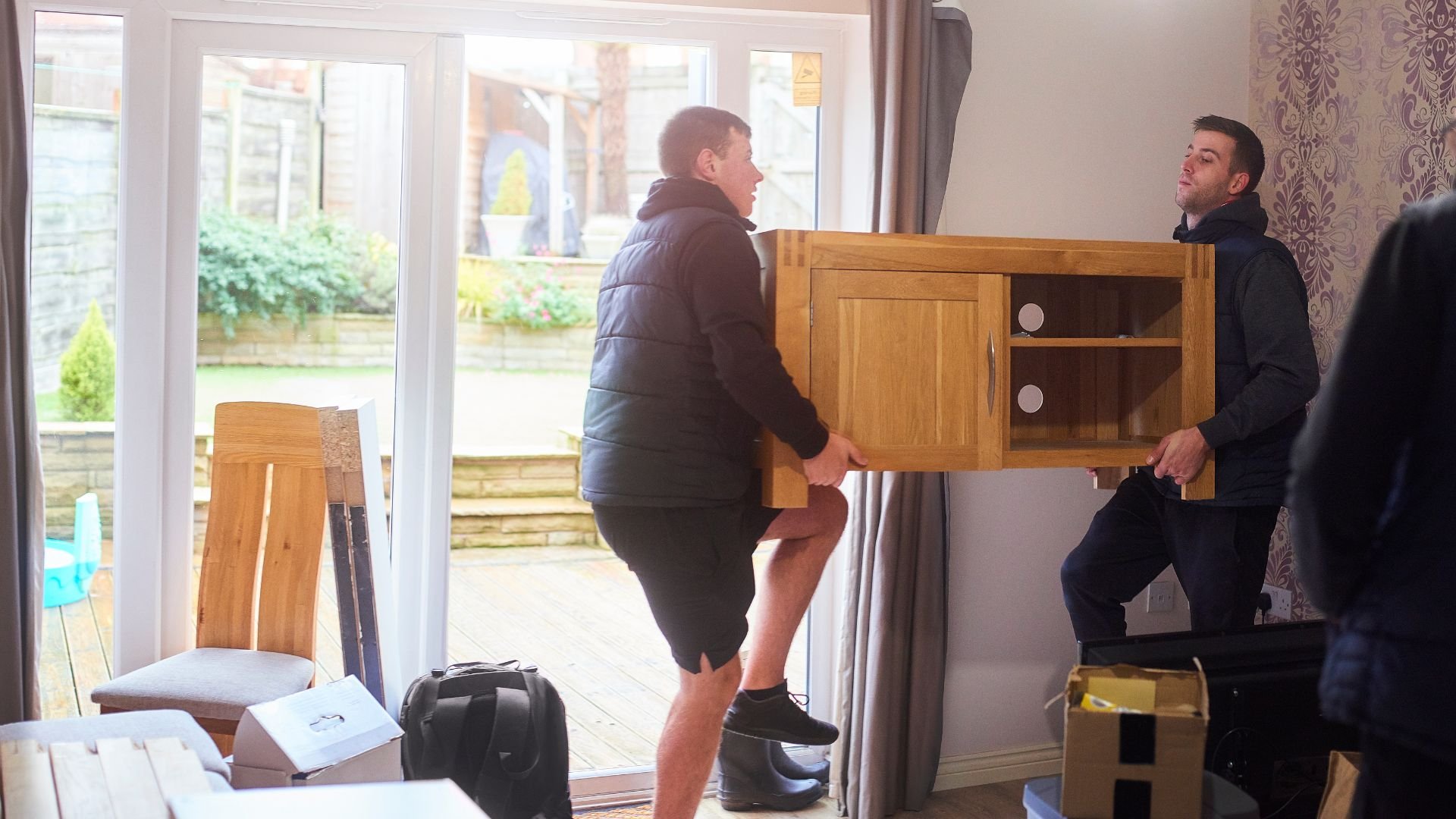 Two men carrying wooden furniture through a doorway during home move