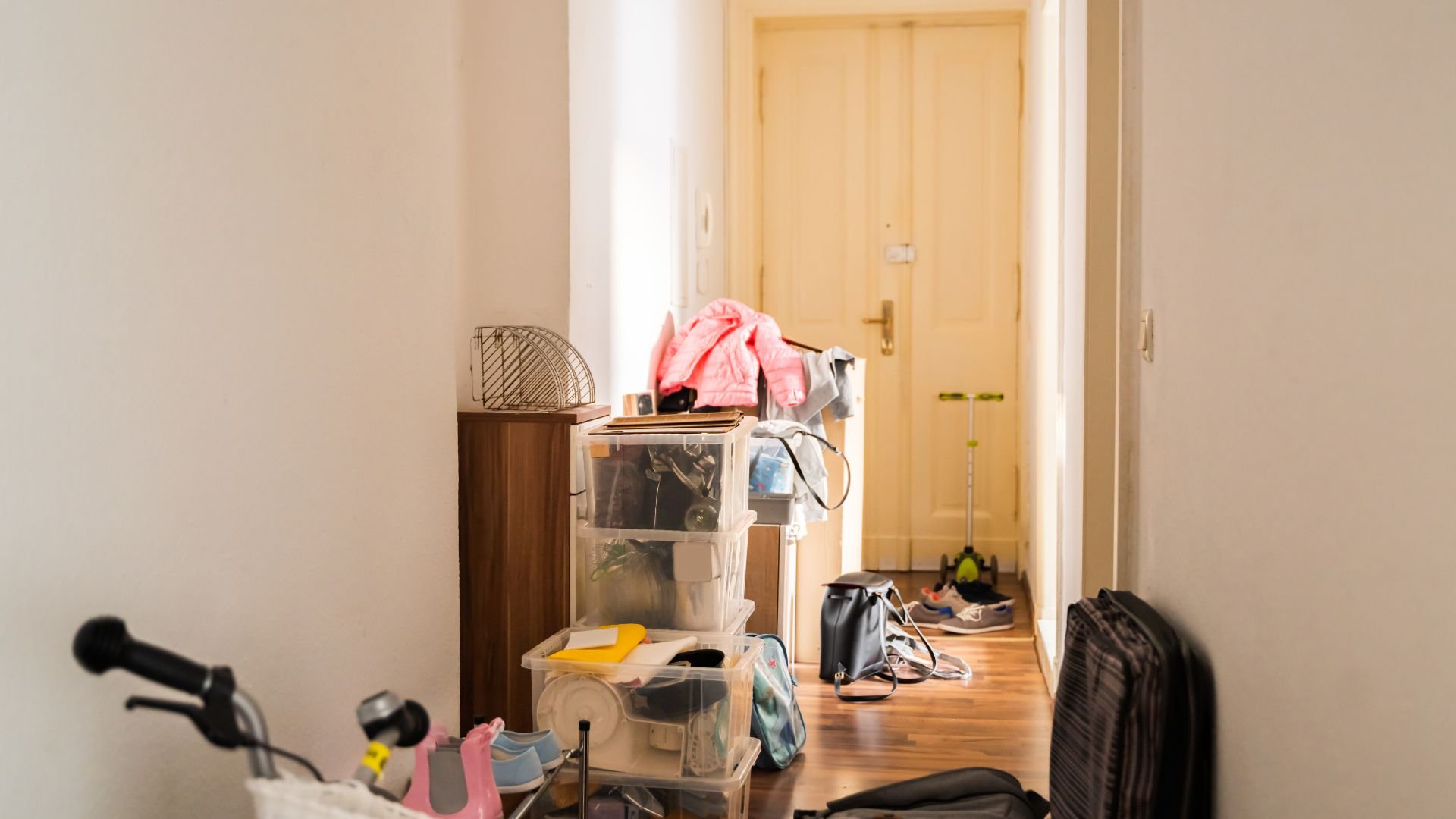 Cluttered room with clear storage boxes, clothes, bike, and wooden door