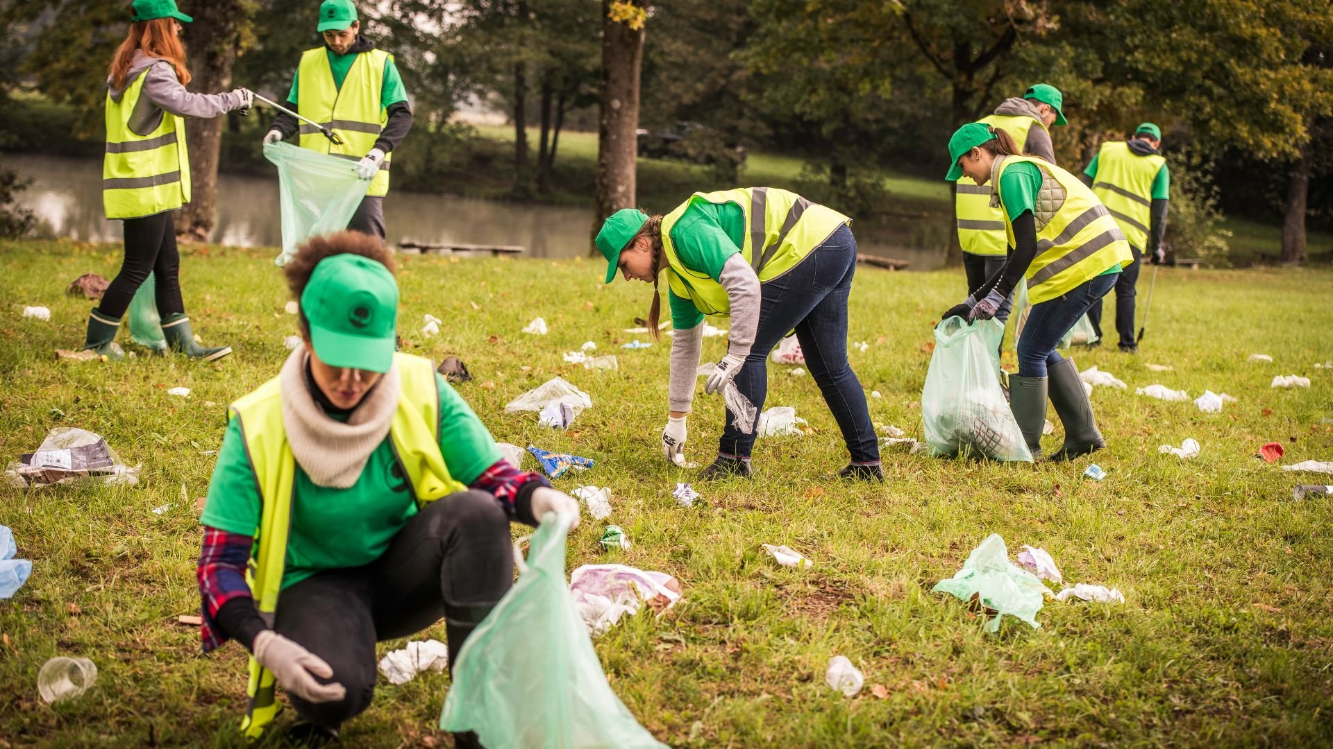 Volunteers in green vests cleaning up litter in a grassy park area