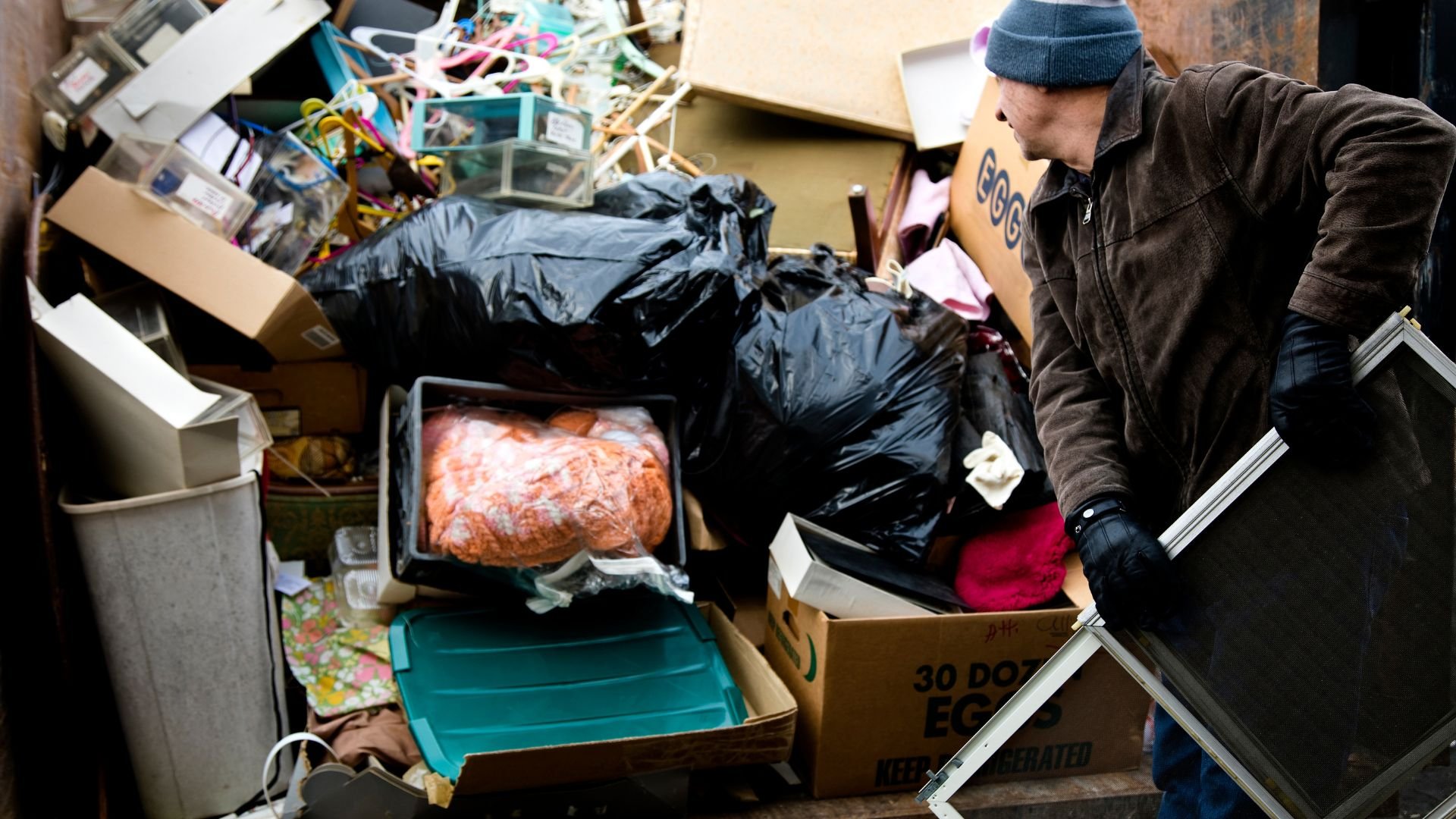 Cluttered storage area with trash bags, boxes, and person sorting items